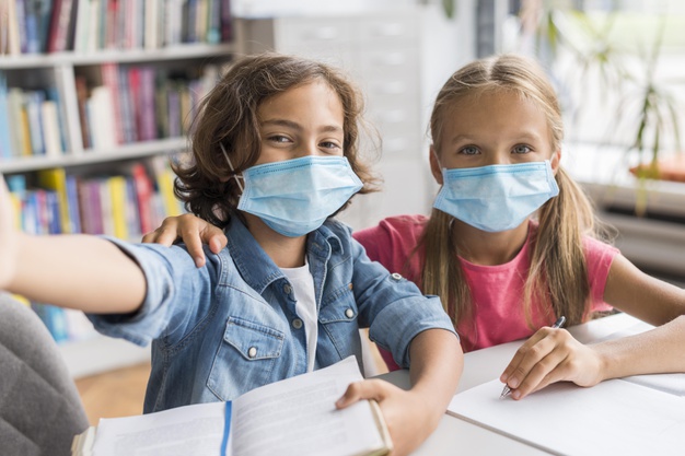 kids-taking-selfie-library-while-wearing-medical-masks_23-2148694844