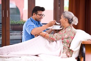 Male nurse feeding food to senior patient on bed